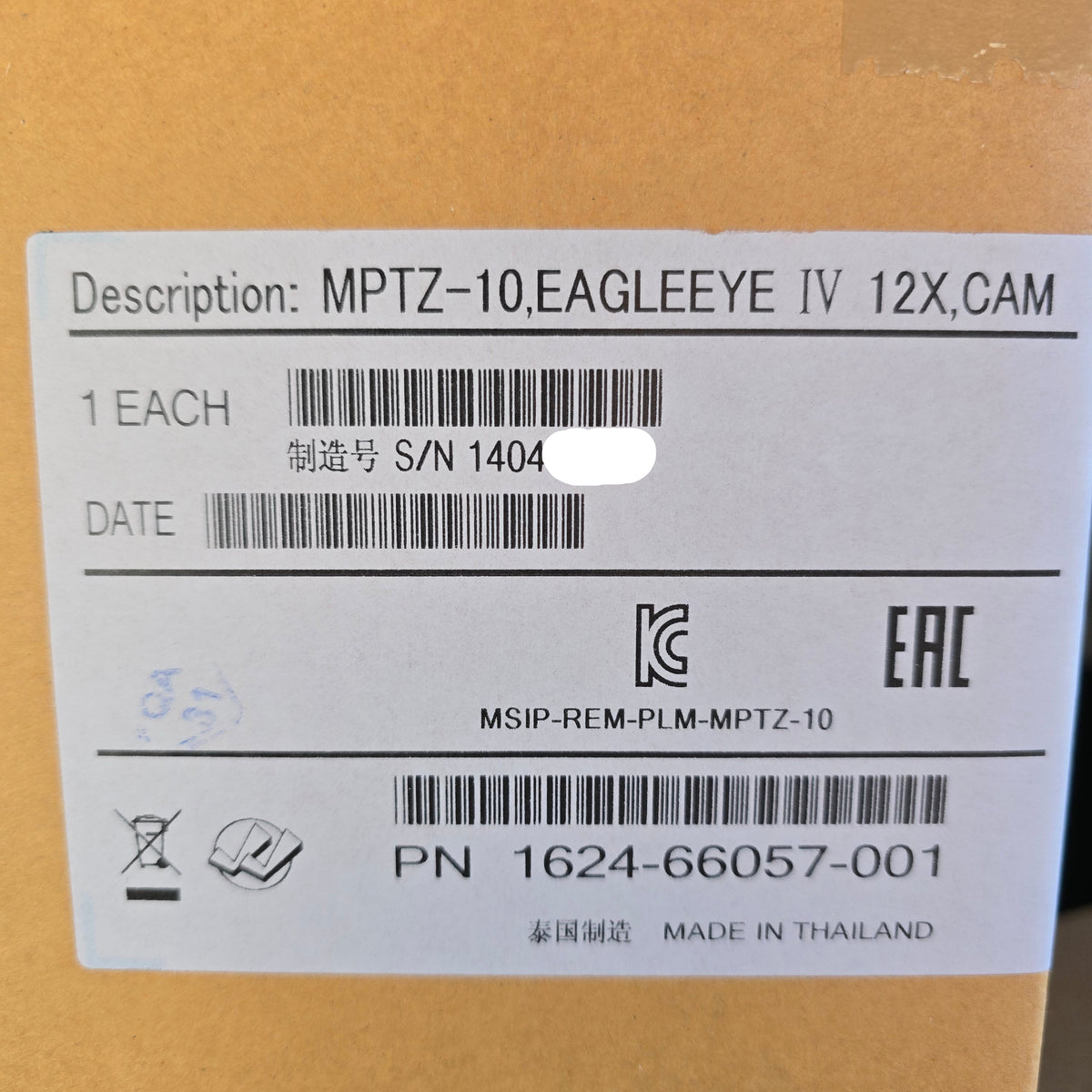 A close-up of a white product label printed with technical specifications and barcodes, attached to a brown cardboard box. The label includes text such as 'Description: MPTZ-10,EAGLEEYE IV 12X,CAM' and 'PN 1624-66057-001'.